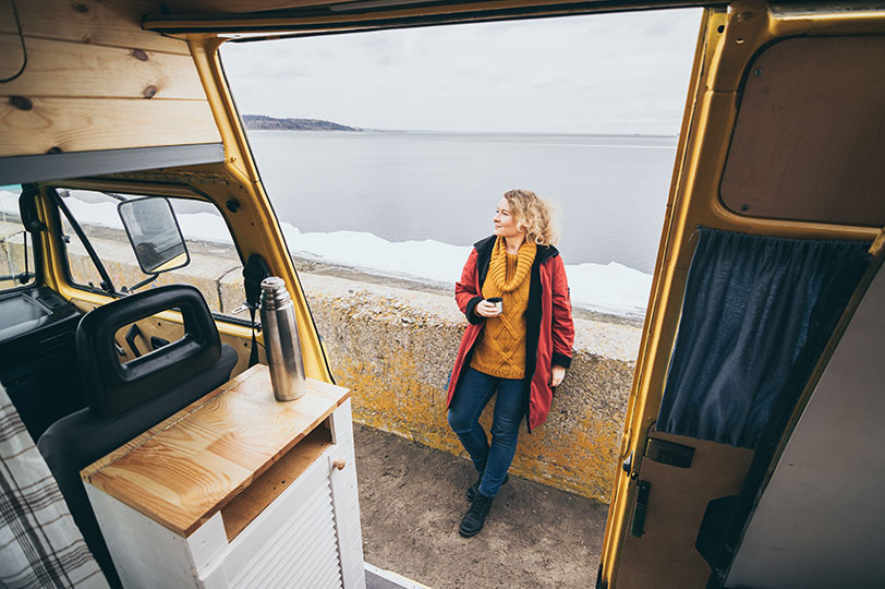 Women drinking a cup of coffee on the sea wall by a campervan