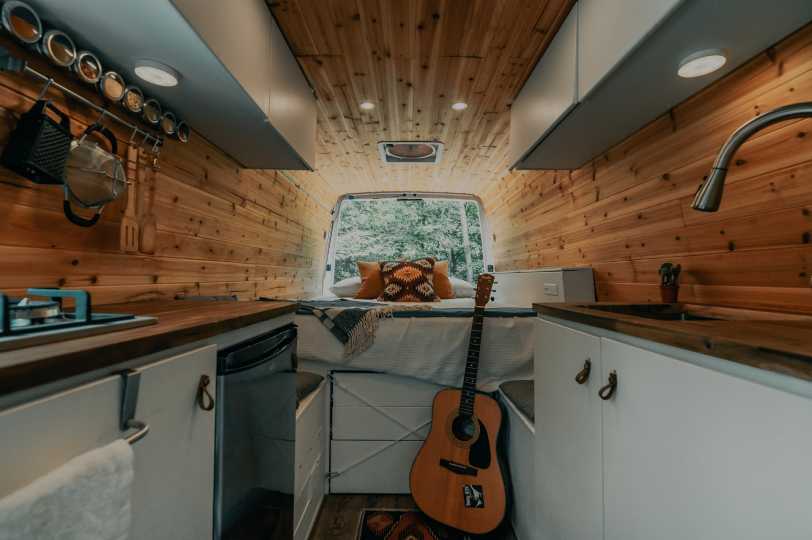 A lovely aesthetic interior of the inside of a campervan using pine wood as the walls and the boot open allowing fresh air and the view inside