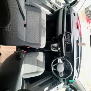 View from the rear of the LWB - T6.1 Volkswagen Transporter Highline Campervan (Pure Grey, DSG, 73 Plate, A1439) shows a modern front interior with grey dashboard, black and silver steering wheel, two grey seats, and gear shift.