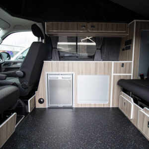 6.1 Volkswagen Transporter Highline Campervan in Pure Grey with the passenger seat swivelled inward with the seats up and the fridge and the storage highlighted