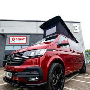 A Fortana Red SWB T6.1 Volkswagen Transporter 150BHP Highline Campervan (23 Plate, A1443) is parked outside a Denby Campervans building, with a large number 3 sign visible on the wall behind it.