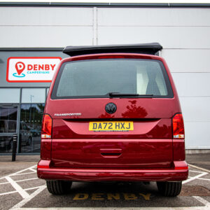 A Fortana Red SWB T6.1 Volkswagen Transporter Highline Campervan (150BHP, MANUAL, 23 Plate, A1443) is parked in a reserved spot outside a Denby Campervans building with the rear facing the camera and the Denby sign visible above.