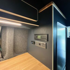 The SWB T6.1 Volkswagen Transporter Highline Campervan (Indium Grey, 73 plate, A1438) features a modern interior with a wooden countertop, digital control panels, electrical outlets, LED under-cabinet lighting, and grey fabric wall lining.