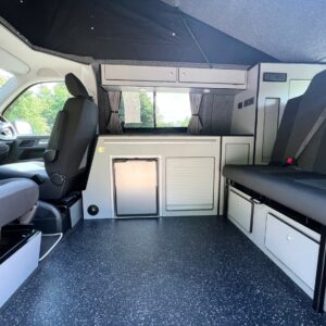The SWB T6.1 Volkswagen Transporter Startline Campervan in Sunny Yellow (71 Plate, A1441) features black and gray seats, storage cabinets, a compact fridge, rear window, and a partially raised roof for extra headroom and natural light.