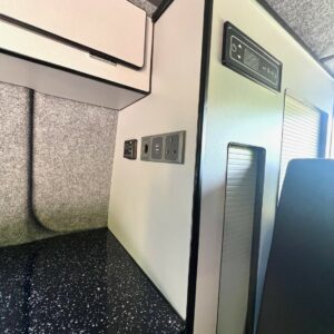 Close-up of the compact kitchen in the SWB T6.1 Volkswagen Transporter Startline Campervan (Sunny Yellow, 71 Plate, A1441) featuring a black speckled countertop, outlets, control panel, light gray cabinets, and textured gray wall.