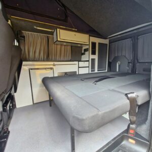 The SWB T6 Volkswagen Transporter Highline Campervan (Deep Black, 17 Plate, A1466) features a folded-down bed, compact kitchenette with fridge, cabinets, drawers, and window curtains for privacy.