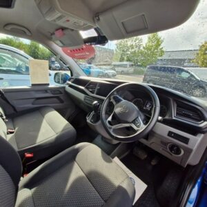 The interior of a Ravenna Blue SWB T6.1 Volkswagen Transporter Highline Campervan (24 plate, Automatic, A1471) features right-hand drive with steering wheel, dashboard, and two front seats. Sunlight streams in; raindrops dot the windscreen.