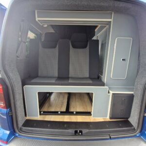 The image shows the interior of a SWB T6.1 Volkswagen Transporter Highline Campervan (Automatic, Ravenna Blue, 24 plate, A1471) with two-tone bench seats, storage compartments, wood-style floor, and open rear doors revealing a modern living area.