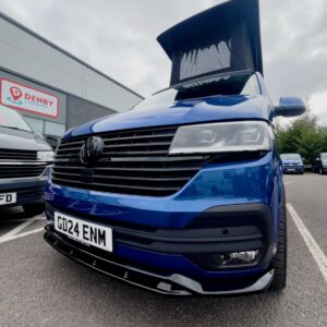 A Ravenna Blue SWB T6.1 Volkswagen Transporter Highline Campervan (Automatic, 24 plate, A1471) is parked outside a Denby building, with other camper vans nearby. License plate: GD24 ENM. Raised pop-up roof visible.